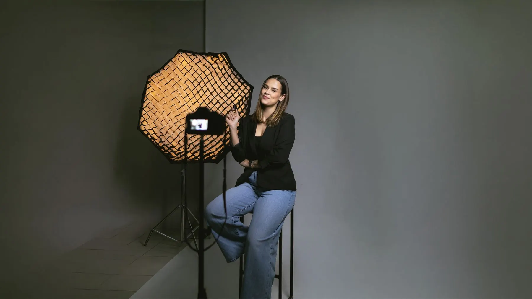 Social media sentada num banco ao lado de um softbox e uma câmera no estúdio