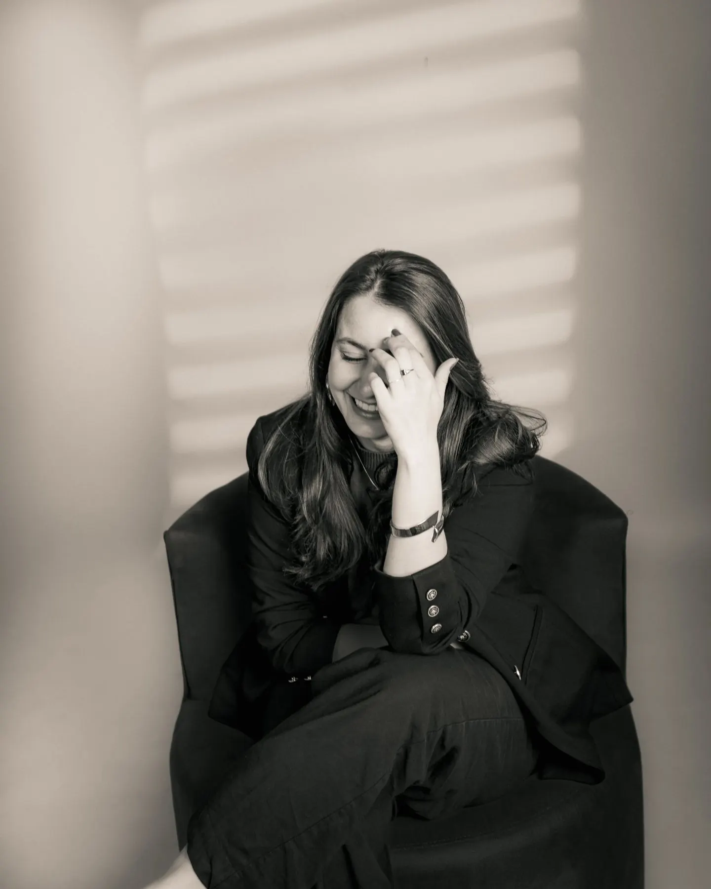 Psicóloga sentada numa poltrona, rindo com a mão no rosto